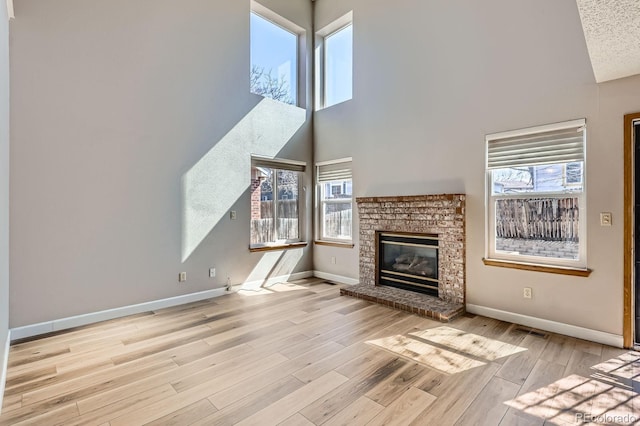 unfurnished living room featuring visible vents, a brick fireplace, baseboards, a high ceiling, and wood finished floors