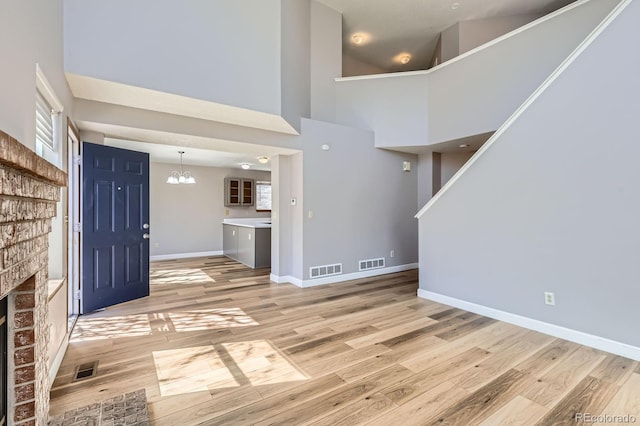 foyer featuring visible vents, light wood-style flooring, a brick fireplace, and baseboards