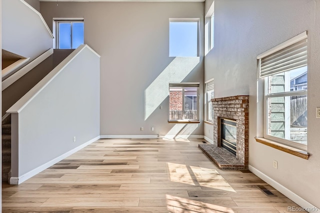 unfurnished living room featuring stairway, a healthy amount of sunlight, a brick fireplace, and wood finished floors