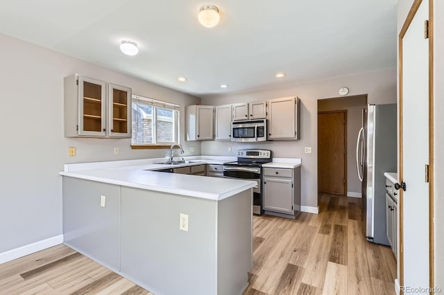 kitchen featuring light wood-type flooring, stainless steel appliances, a peninsula, and a sink