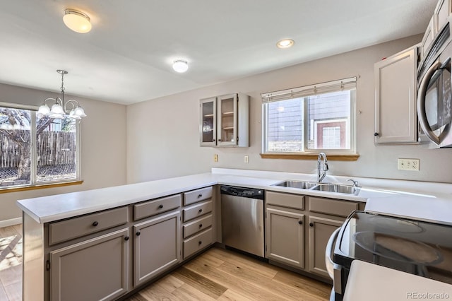 kitchen with a peninsula, light wood-style flooring, gray cabinets, a sink, and dishwasher