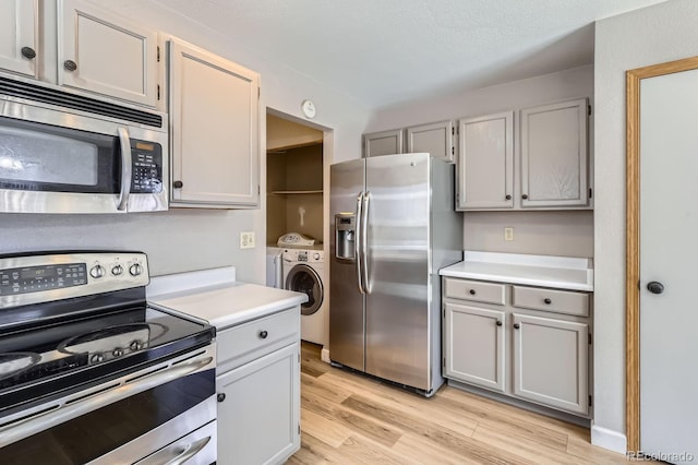 kitchen with light wood-type flooring, washer and dryer, stainless steel appliances, and light countertops