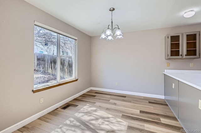 unfurnished dining area featuring visible vents, baseboards, light wood-style floors, and a chandelier