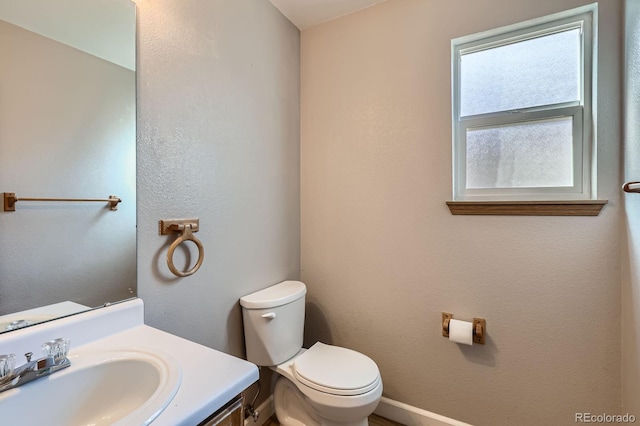 half bath featuring toilet, vanity, and a textured wall