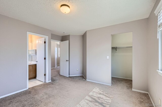 unfurnished bedroom featuring a walk in closet, light carpet, a textured ceiling, and baseboards