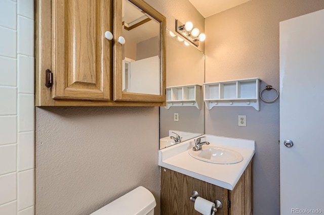 bathroom with toilet, vanity, and a textured wall