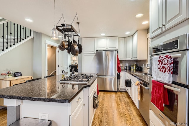 kitchen featuring light wood finished floors, white cabinets, appliances with stainless steel finishes, tasteful backsplash, and a center island