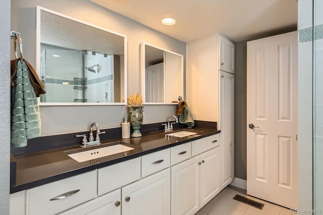 bathroom featuring double vanity, visible vents, walk in shower, and a sink