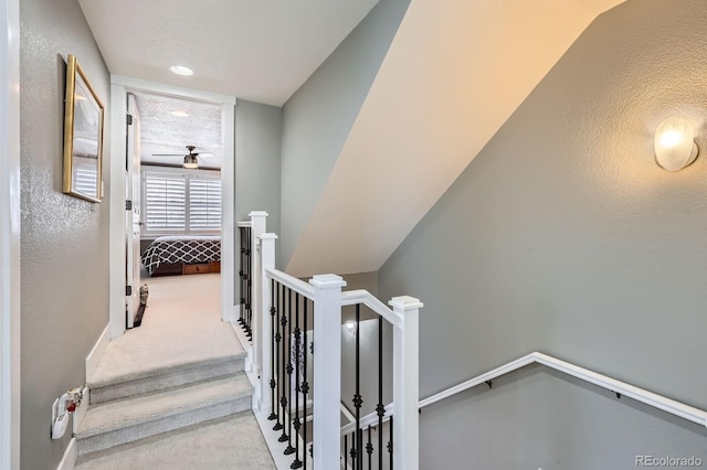 stairway with a ceiling fan, carpet flooring, and a textured wall