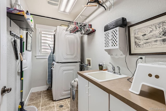 laundry area with visible vents, light tile patterned floors, stacked washer and clothes dryer, cabinet space, and a sink