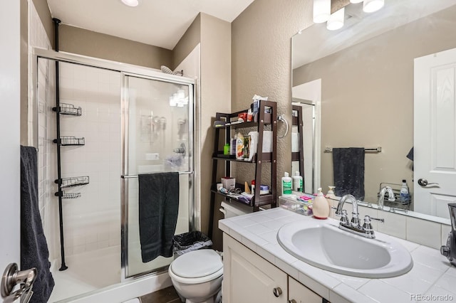 full bathroom featuring toilet, a stall shower, vanity, and a textured wall