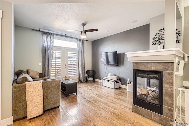 living area with a ceiling fan, wood finished floors, baseboards, a textured ceiling, and a tiled fireplace