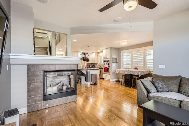 living area featuring a textured ceiling, baseboards, light wood-type flooring, and ceiling fan