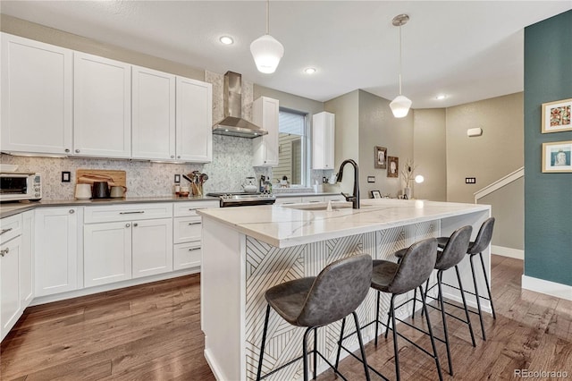 kitchen featuring decorative backsplash, light stone countertops, wall chimney range hood, and wood finished floors