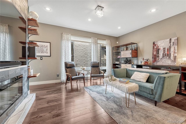 living room featuring a glass covered fireplace, baseboards, wood finished floors, and recessed lighting