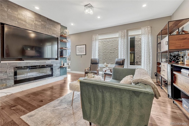 living room featuring a glass covered fireplace, baseboards, wood finished floors, and recessed lighting