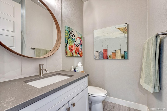 bathroom with baseboards, toilet, wood finished floors, and vanity