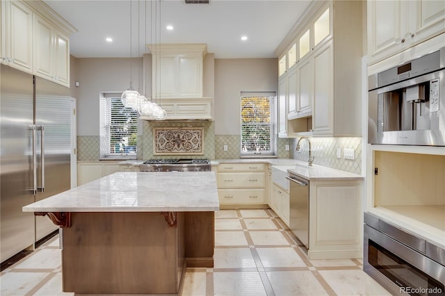 kitchen with a center island, backsplash, built in appliances, light stone countertops, and decorative light fixtures