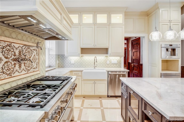 kitchen with hanging light fixtures, sink, appliances with stainless steel finishes, light stone counters, and custom range hood