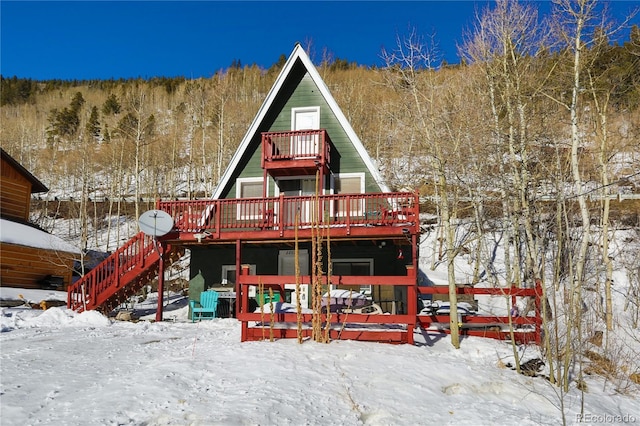 snow covered house featuring a forest view, stairway, and a deck