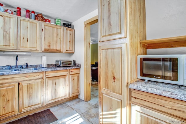 kitchen with light stone countertops, a toaster, a sink, and light brown cabinetry