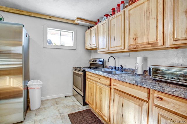 kitchen with light tile patterned floors, dark countertops, stainless steel appliances, light brown cabinets, and a sink