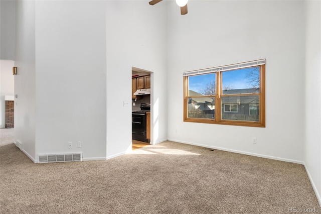 unfurnished living room featuring a towering ceiling, ceiling fan, and carpet