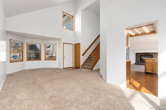 unfurnished living room with a brick fireplace, light colored carpet, and high vaulted ceiling