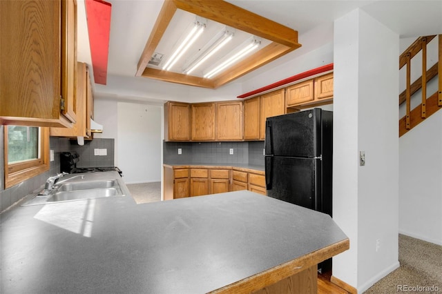 kitchen featuring black refrigerator, tasteful backsplash, sink, stove, and kitchen peninsula