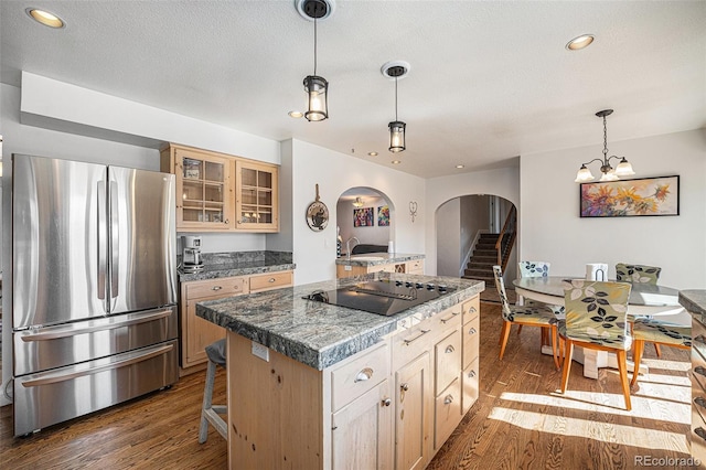 kitchen featuring wood-type flooring, a kitchen island, stainless steel fridge, black electric cooktop, and a breakfast bar area