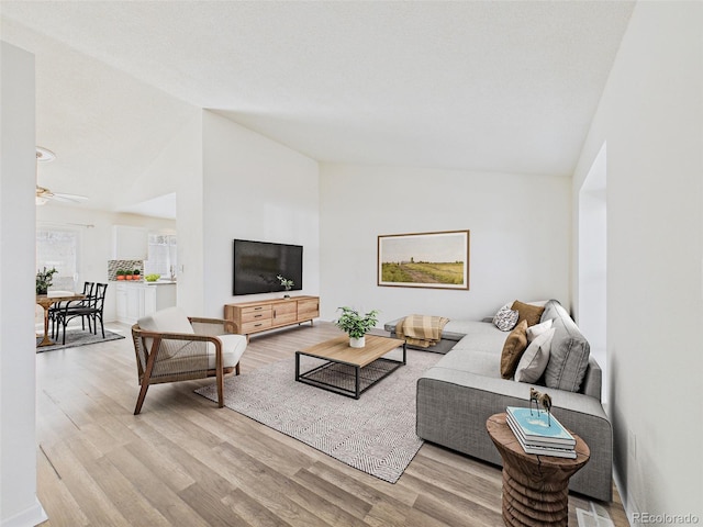 living area featuring a ceiling fan, light wood-style floors, and lofted ceiling