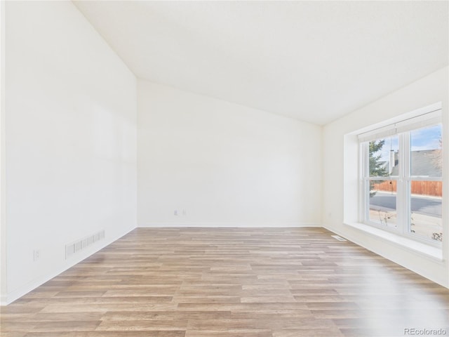 spare room featuring light wood-type flooring, visible vents, and lofted ceiling