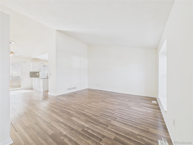 unfurnished living room with ceiling fan, visible vents, lofted ceiling, and light wood-style flooring