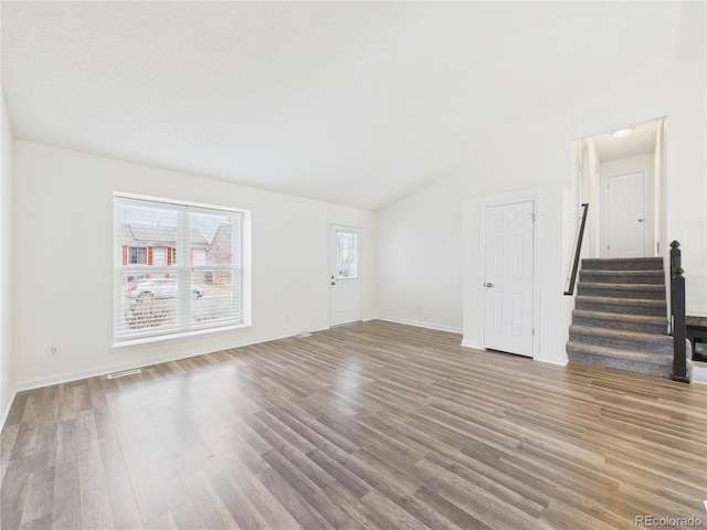 unfurnished living room with visible vents, baseboards, stairway, lofted ceiling, and wood finished floors