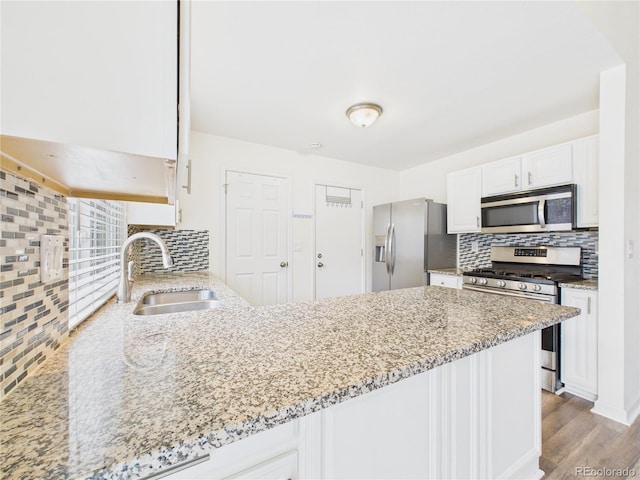 kitchen featuring white cabinets, appliances with stainless steel finishes, light stone countertops, and a sink