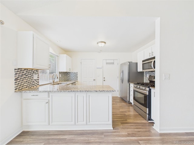 kitchen with light stone counters, a peninsula, a sink, appliances with stainless steel finishes, and tasteful backsplash