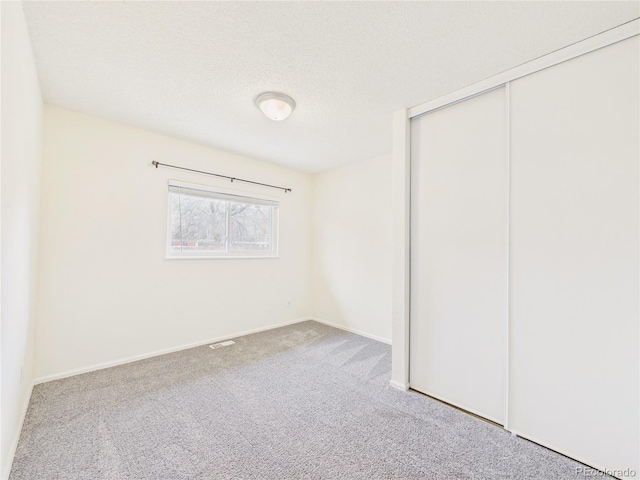 unfurnished bedroom featuring a closet, a textured ceiling, baseboards, and carpet floors