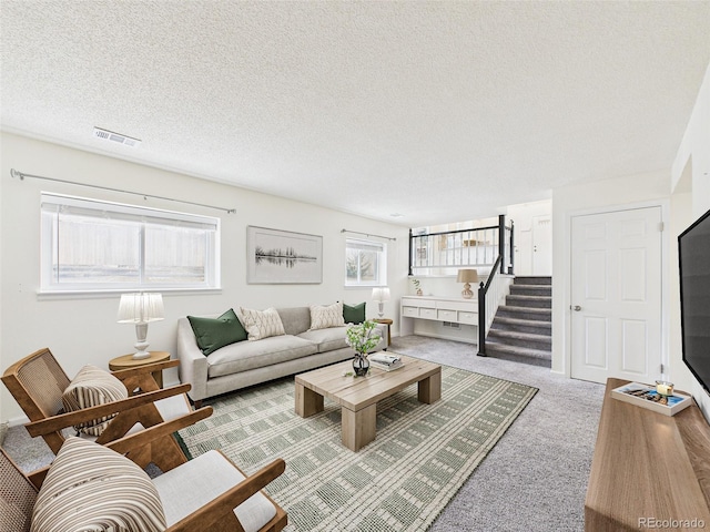 carpeted living area with stairs, visible vents, and a textured ceiling