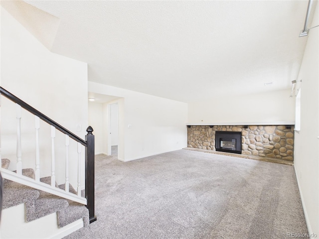 unfurnished living room featuring a stone fireplace, stairway, baseboards, and carpet floors