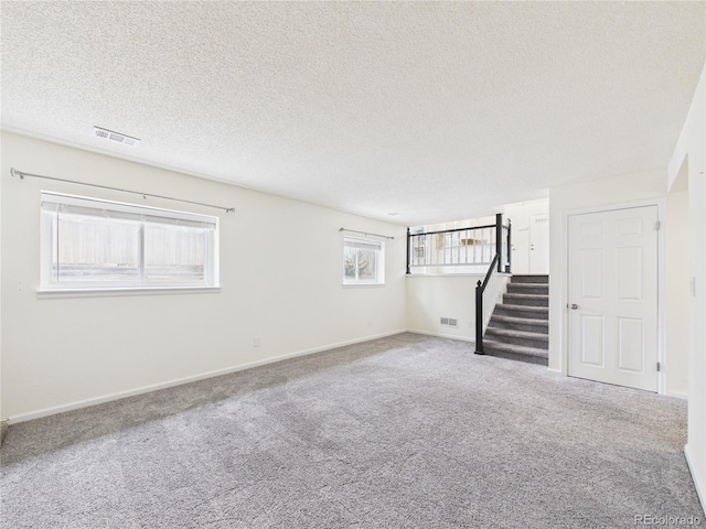 carpeted empty room featuring baseboards, stairway, a textured ceiling, and visible vents