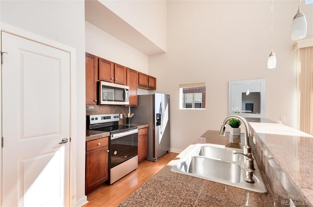 kitchen with pendant lighting, sink, light hardwood / wood-style flooring, appliances with stainless steel finishes, and a towering ceiling