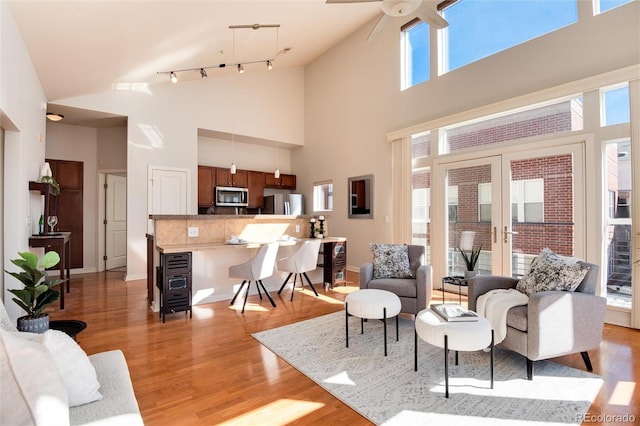 living room featuring ceiling fan, light hardwood / wood-style flooring, high vaulted ceiling, and a healthy amount of sunlight