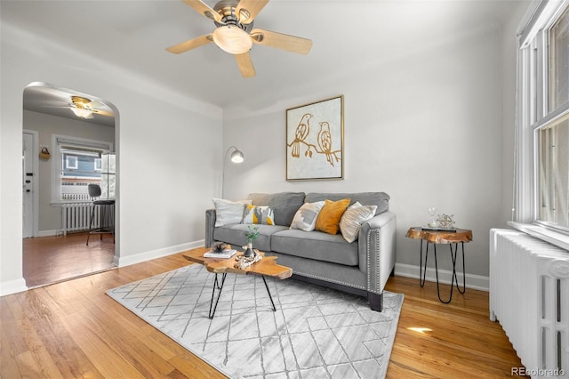 2616 Utica St, Denver, CO 80212 - living room featuring radiator heating unit, a ceiling fan, arched walkways, and light wood-style flooring
