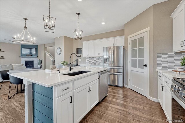 kitchen with stainless steel appliances, light wood-style floors, a large fireplace, and a sink