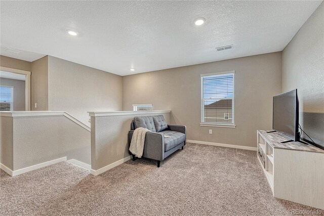 living area featuring light carpet, baseboards, visible vents, and an upstairs landing