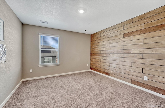 empty room featuring a textured ceiling, a textured wall, carpet floors, wood walls, and baseboards