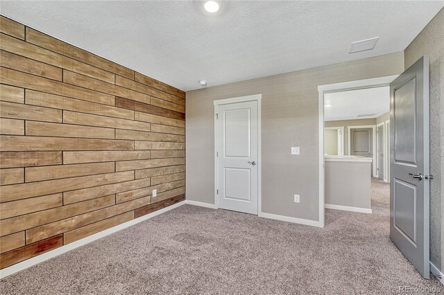 unfurnished bedroom featuring carpet floors, baseboards, wooden walls, and a textured ceiling