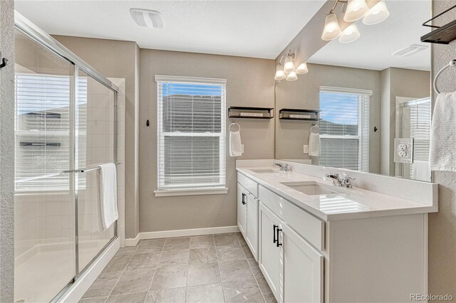 full bath featuring double vanity, a stall shower, baseboards, and a sink