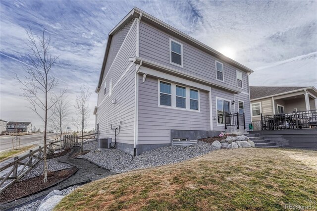 rear view of property featuring central AC, fence, a wooden deck, and a lawn