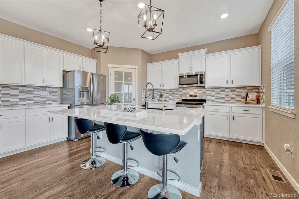 kitchen featuring visible vents, appliances with stainless steel finishes, wood finished floors, light countertops, and a sink
